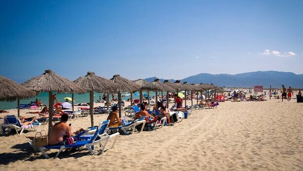 Una spiaggia con lettini e ombrelloni di paglia sotto un cielo sereno.