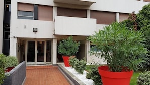 Un edificio moderno con un ingresso piastrellato, grandi piante in vaso e un vialetto in mattoni che conduce all'ingresso.