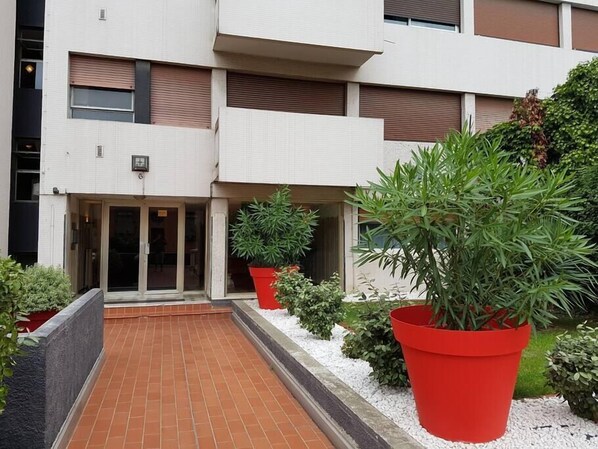 A modern building with a tiled entrance, large potted plants, and a brick pathway leading to the entrance.