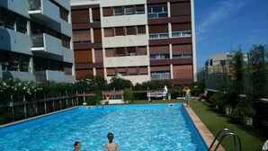 Una piscina con due persone che nuotano, circondata da un edificio a più piani con balconi.