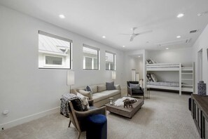 A modern, well-lit living room with a sofa, a coffee table, a chair, a bunk bed, and a ceiling fan. - LBJ Lake Lounging-Lakefront w/ Private Heated Pool (Kingsland)