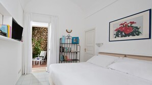 Un dormitorio con cama, estantería, televisor y puerta que da a un balcón.