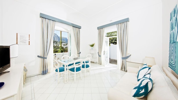 Un salón amplio y luminoso con comedor, muebles blancos y ventanas grandes con cortinas.