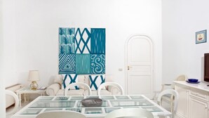Un comedor con una mesa de vidrio, sillas blancas y un cuadro abstracto grande en la pared.