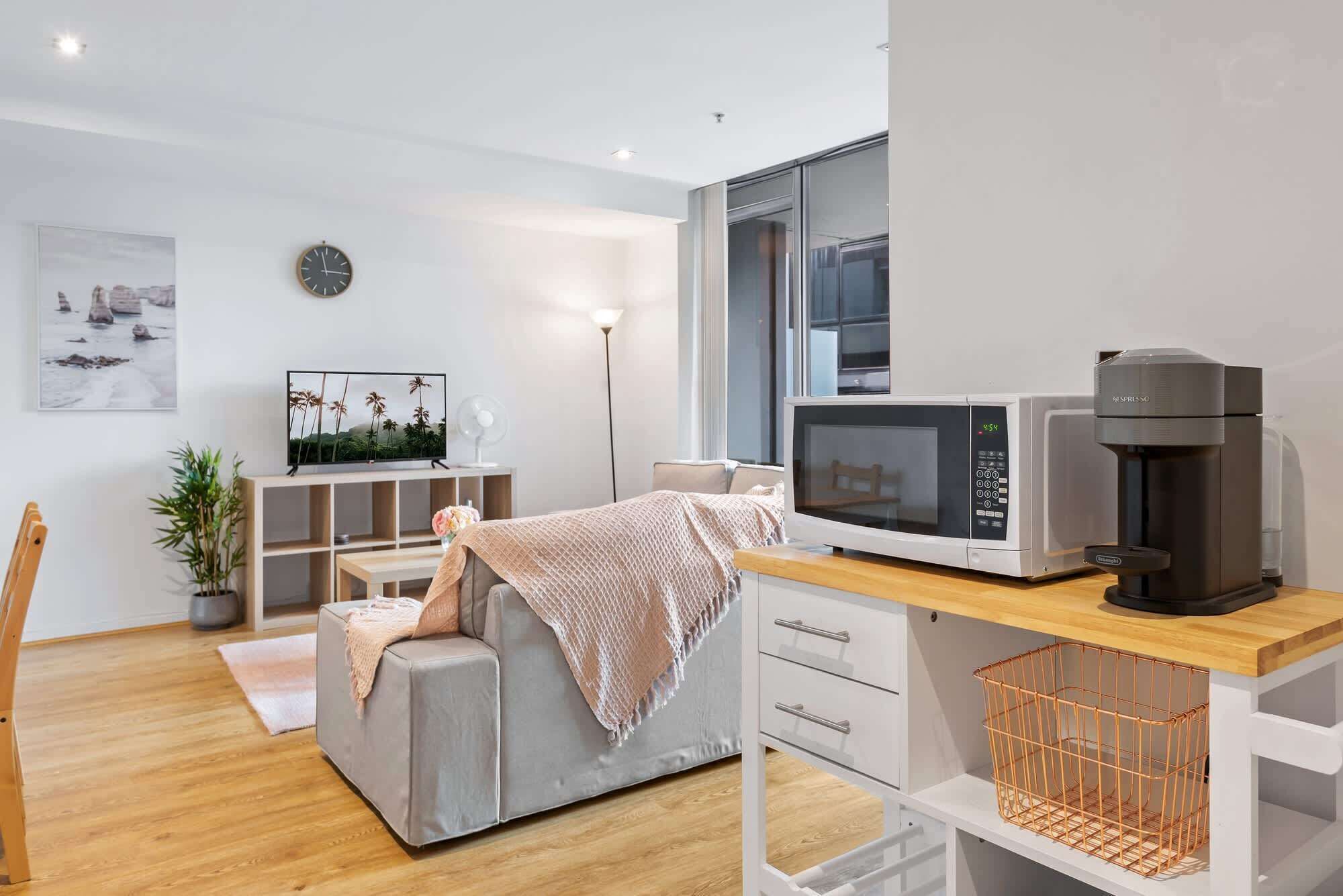 Ein modernes, kompaktes Wohnzimmer mit einer Couch, einem Fernseher, einer Mikrowelle und einer Kaffeemaschine.