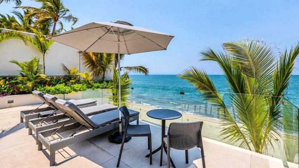 A balcony with lounge chairs, a table, and an umbrella overlooking the ocean. - CDM 205: Beachfront 2BR w Pool, Gym & Ocean Views (Bucerías)