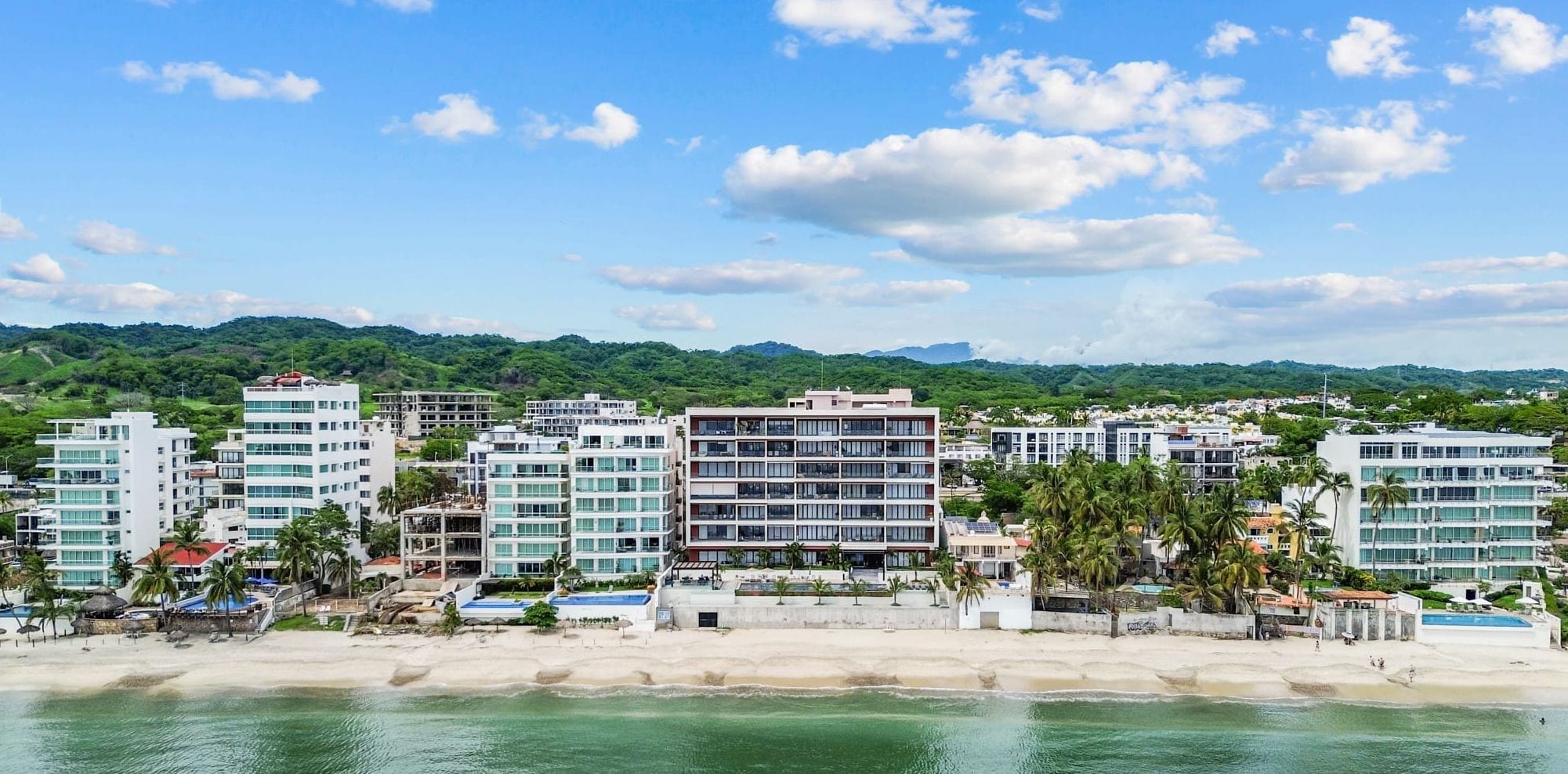 Eine Küstenstadt mit modernen Gebäuden, einem Strand und einem bergigen Hintergrund.