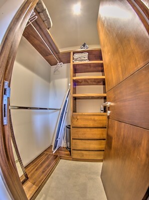 Ein kompakter Kleiderschrank mit Holzoptik, eingebauten Regalen und einer Kleiderstange, mit einem kleinen zusammengefalteten Handtuch obenauf.