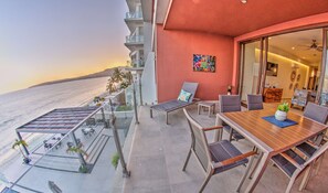 A balcony with a view of the ocean, a dining table with chairs, and a lounge chair. - CDM 205: Beachfront 2BR w Pool, Gym & Ocean Views (Bucerías)