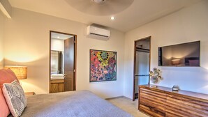 A bedroom with a bed, a dresser, a mirror, an air conditioning unit, and a colorful abstract painting. - CDM 205: Beachfront 2BR w Pool, Gym & Ocean Views (Bucerías)