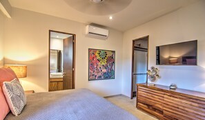 A bedroom with a bed, a dresser, a mirror, an air conditioning unit, and a colorful abstract painting. - CDM 205: Beachfront 2BR w Pool, Gym & Ocean Views (Bucerías)
