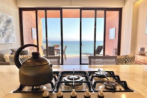 A kitchen with a gas stove, a kettle, and a view of the sea through large sliding doors.
