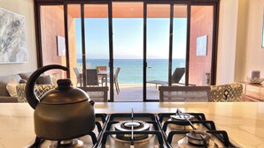 A kitchen with a gas stove, a kettle, and a view of the sea through large sliding doors. - CDM 205: Beachfront 2BR w Pool, Gym & Ocean Views (Bucerías)