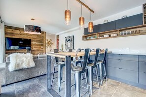 Eine moderne Küche mit einer Wand in Holzoptik, einem Essbereich mit Metallstühlen und Pendelleuchten.