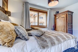 Ein Schlafzimmer mit einem großen Bett, einem Holzschrank und einem Fenster mit Blick auf ein Holzhaus.