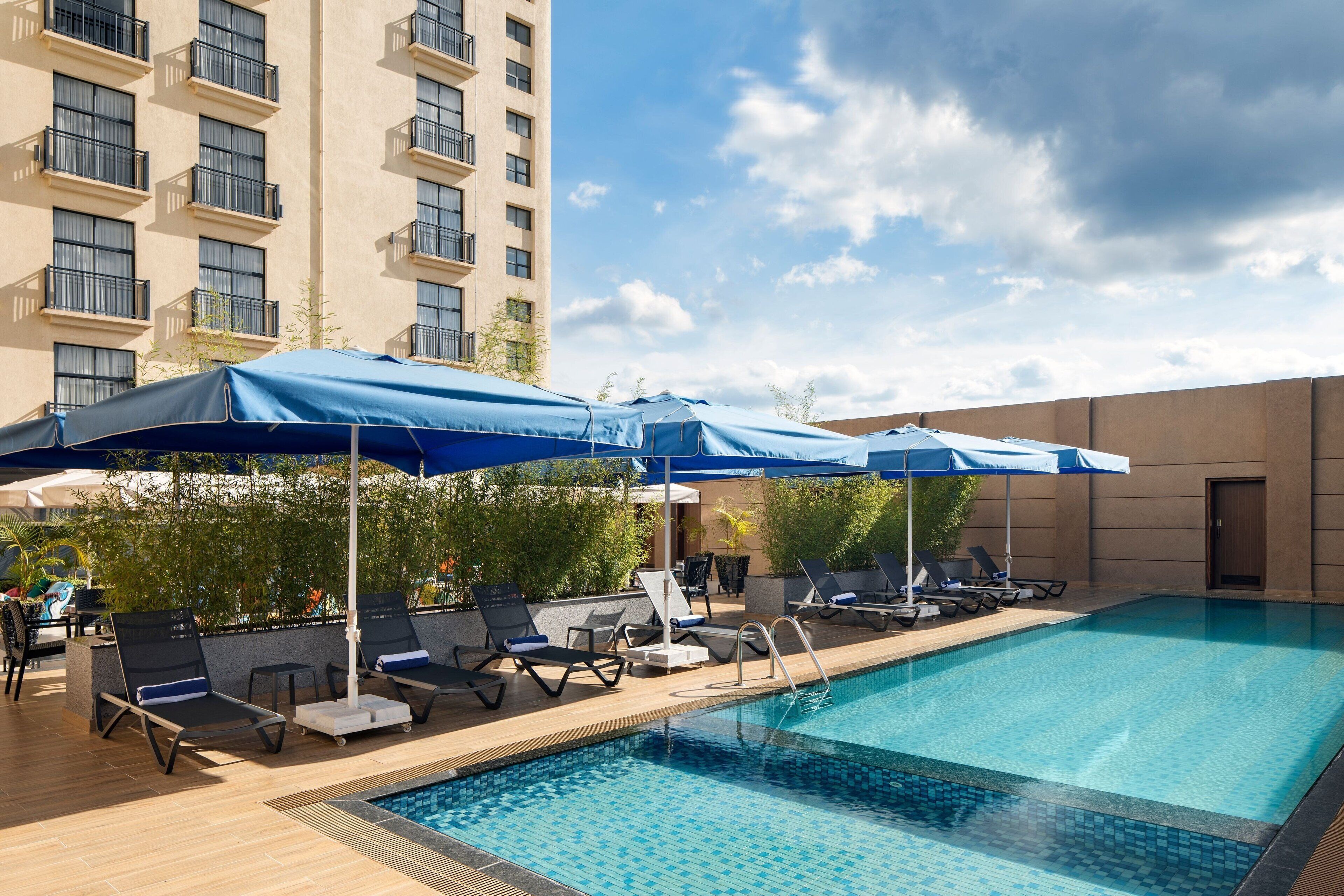 A rooftop pool with lounge chairs and umbrellas, surrounded by a high-rise building.