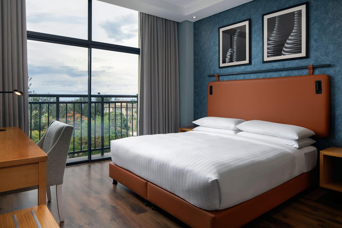 Una habitación de hotel moderna con una cama grande, un escritorio y vistas al exterior desde un balcón.