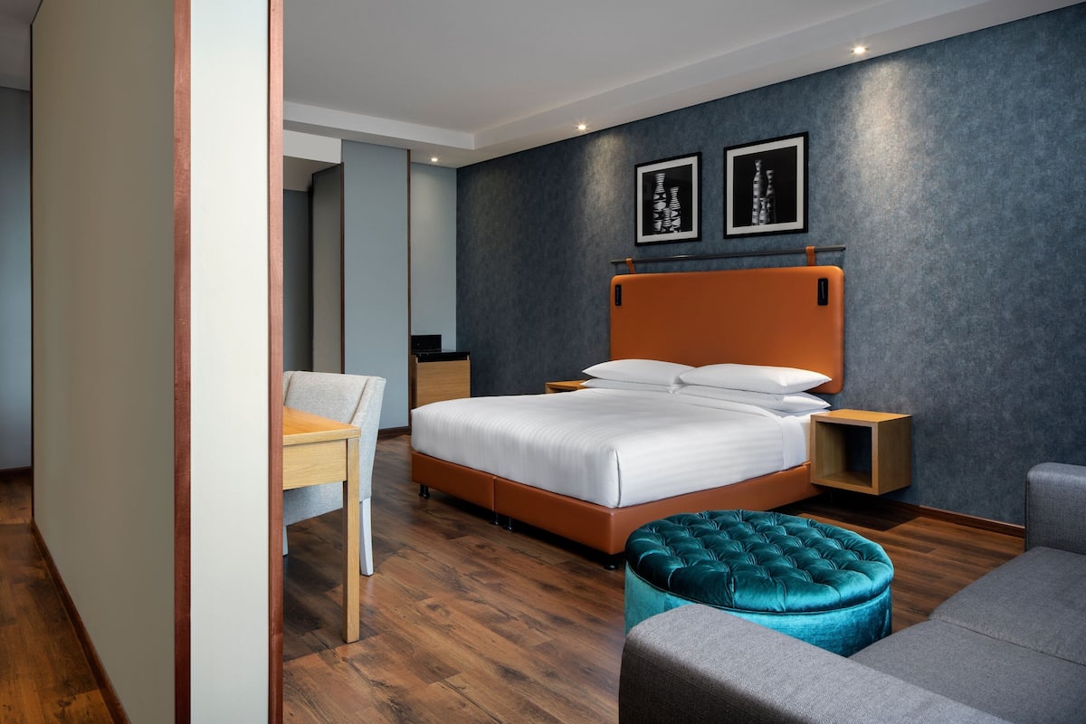 Una habitación de hotel moderna con una cama grande, un escritorio, una silla y un otoman tapizado.
