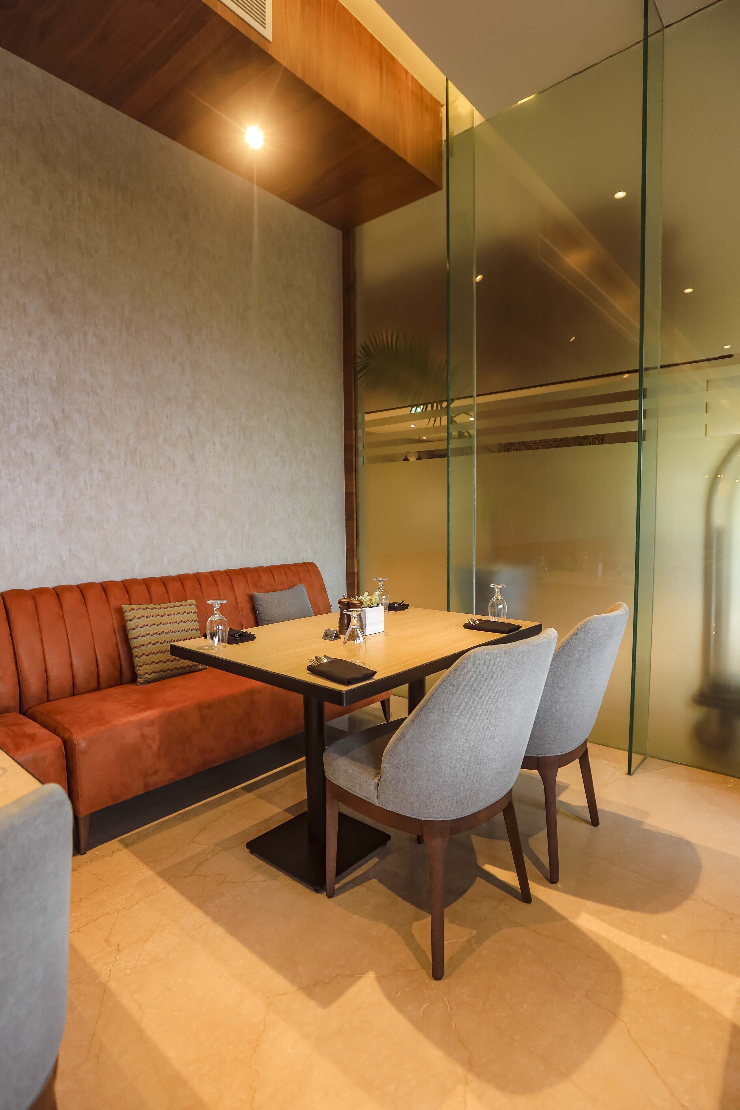A modern interior with a wooden ceiling, a glass partition, a sofa, a table with chairs, and a small plant.