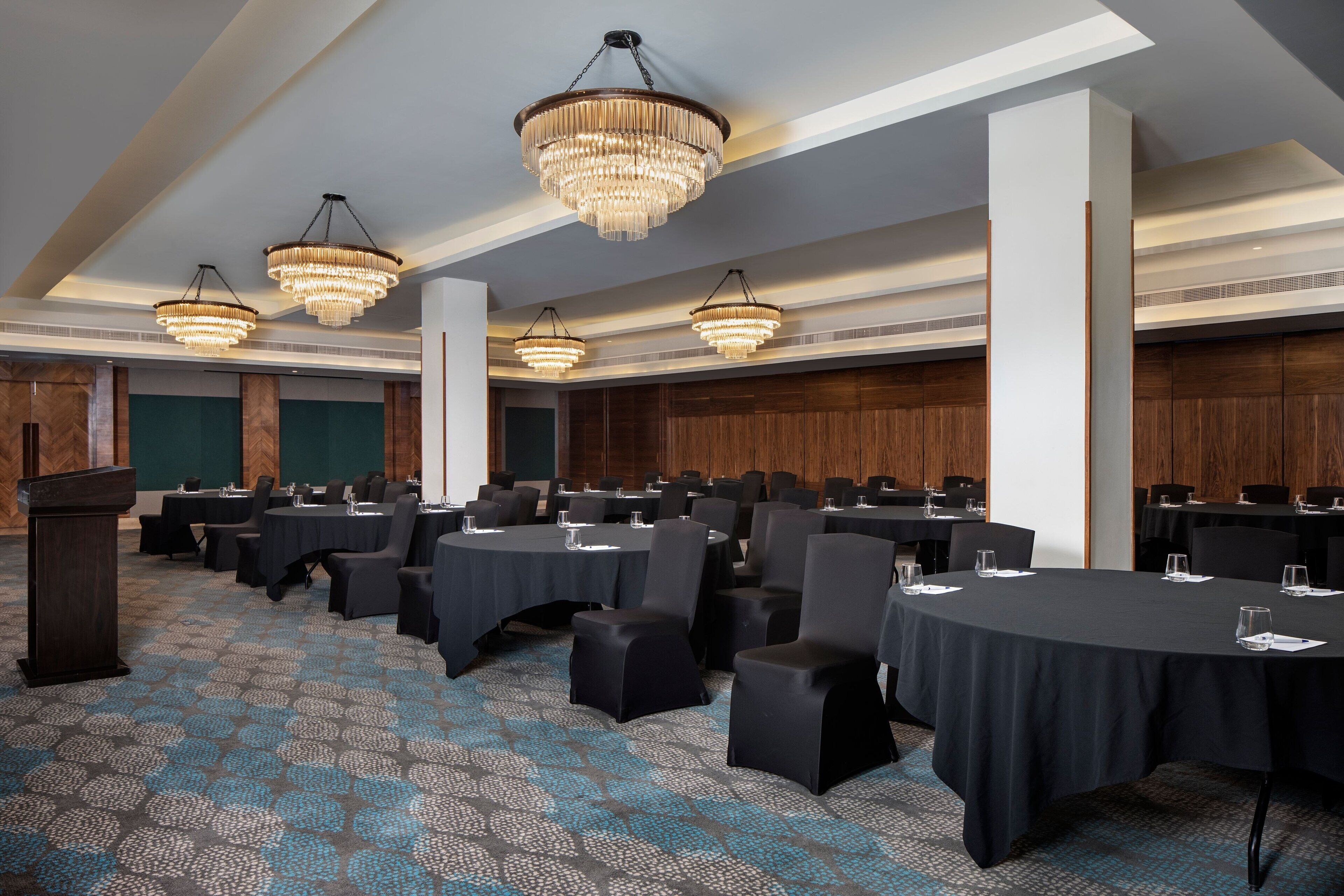 A conference room with round tables, black chairs, and chandeliers.