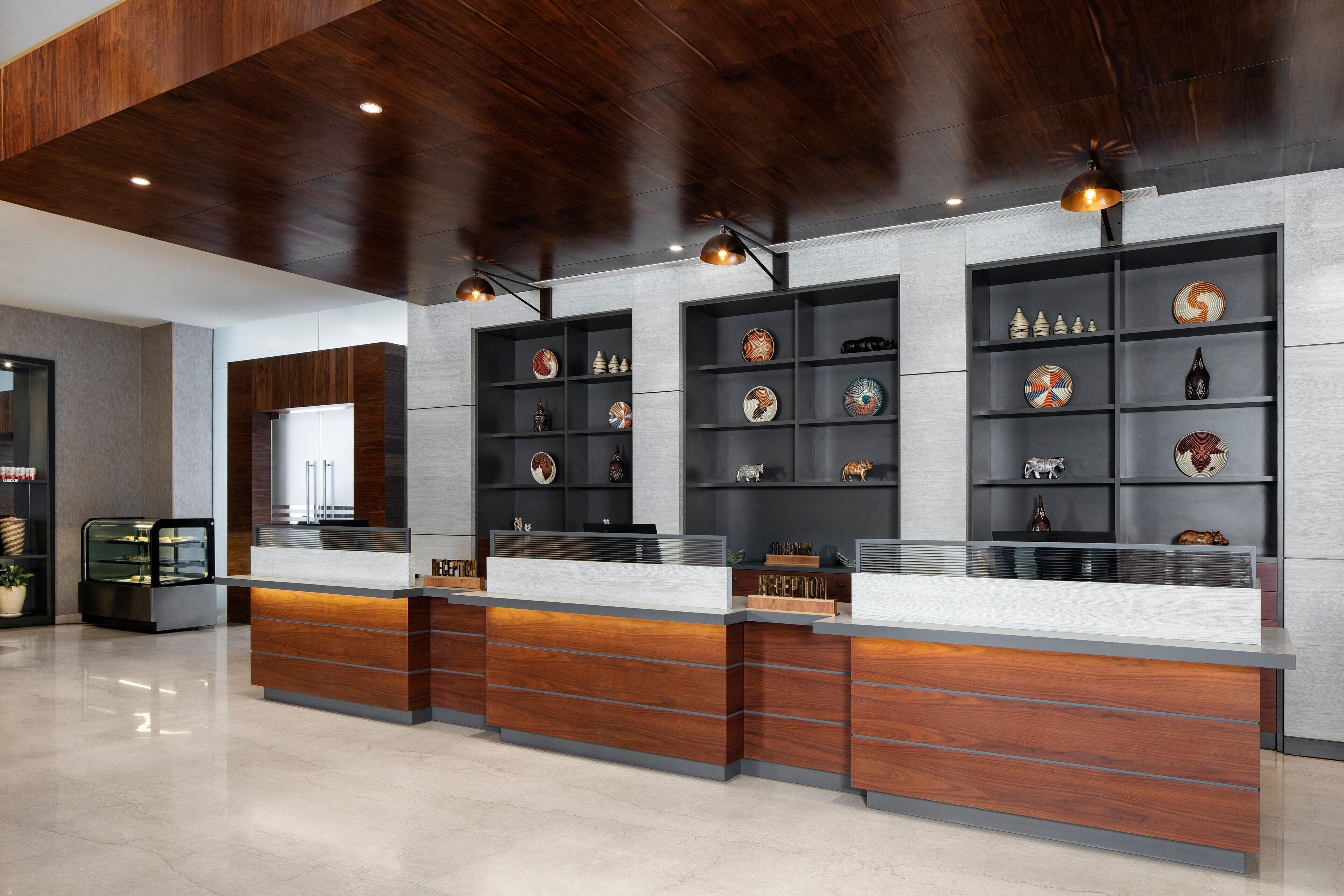 A reception area with a wooden reception desk, shelves with decorative items, and a modern ceiling design.
