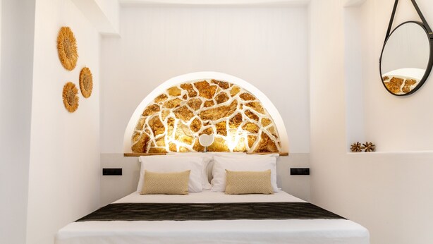 A modern bedroom with a unique ceiling design, a bed with white linens, and a wall-mounted mirror. - Camares of Castle - Room 2 (Naxos)