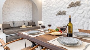 A dining area with a table set for four, including plates, glasses, and a bottle of wine. A sofa and a decorative wall are in the background. - Camares of Castle - Room 2 (Naxos)