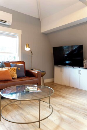 A modern living room with a leather sofa, a glass coffee table, a flat-screen TV, and a floor lamp.