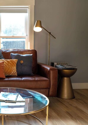 A living room with a brown leather sofa, a glass coffee table, a floor lamp, and a radiator.