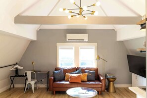 A loft-style living room with a brown leather sofa, a round coffee table, and a modern chandelier. - Modern Carriage House | Prime Location • Parking (Indianapolis)