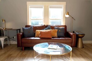 A living room with a brown leather sofa, a glass coffee table, and a lamp. - Modern Carriage House | Prime Location • Parking (Indianapolis)