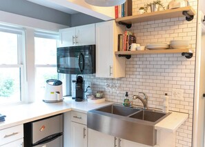 A modern kitchen with white cabinetry, a stainless steel sink, a black microwave, and a coffee maker. - Modern Carriage House | Prime Location • Parking (Indianapolis)