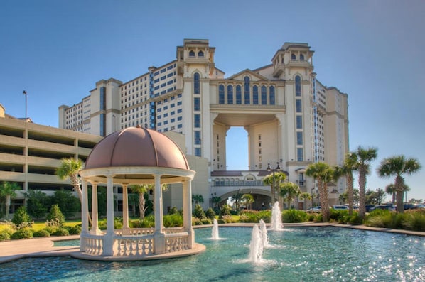 A hotel with a large fountain, a gazebo, and a prominent archway.