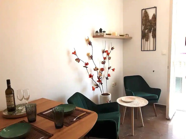 A dining area with a wooden table, green chairs, a vase with red flowers, and a small shelf with decorative items.