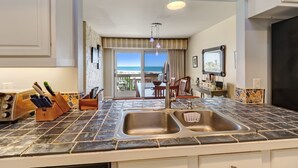 A kitchen with a large window, a sink, and a dining area with a view of the sea. - Oceanfront 2 Bedroom/2 Bath Windsong (Fernandina Beach)