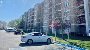A multi-story residential building with balconies, a parking lot, and a tree with pink blossoms.