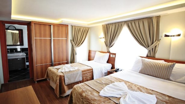 A hotel room with two beds, a wooden wardrobe, a bathroom with a sink, and curtains. - Taksim Palace Hotel Apart  (Istanbul)