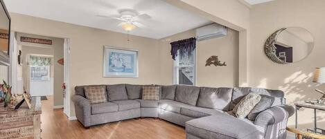 A spacious living room with a large L-shaped sectional sofa, a ceiling fan, and a framed artwork on the wall.