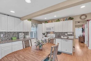 Una cucina moderna con pensili bianchi, un tavolo da pranzo in legno e uno schienale piastrellato.