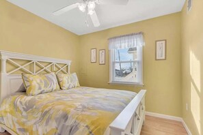 Una camera da letto con un letto, una ventola a soffitto, una finestra con persiane e quadri appesi al muro.