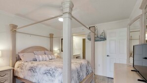 A four-poster bed with a marble-patterned bedspread, a bedside table with drawers, a mirror, and a television on a wooden dresser. - Amazing 2 bedroom unit located on golf course near Siesta Key Beaches (Sarasota)