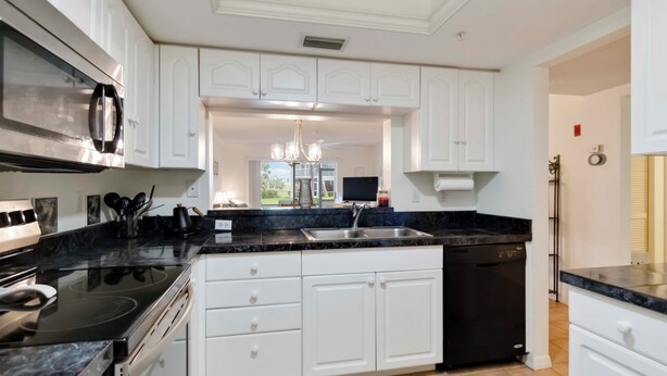 A modern kitchen with white cabinetry, a black countertop, and stainless steel appliances. - Amazing 2 bedroom unit located on golf course near Siesta Key Beaches (Sarasota)