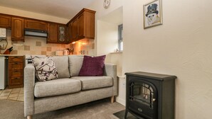 A cozy living room with a sofa, a fireplace, wooden cabinets, and a kitchen in the background.