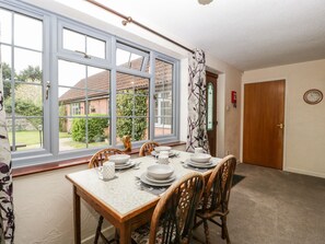 A dining area with a table set for four, large windows, and a view of a garden. - Owls Retreat (Weston-super-Mare)