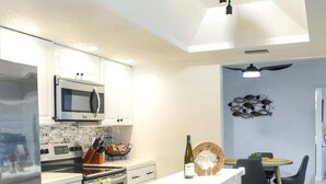 Uma cozinha moderna com armários brancos, micro-ondas embutido e uma ilha central com gavetas.