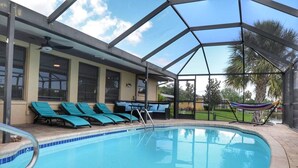 Uma área de piscina com estrutura envidraçada, espreguiçadeiras azuis e uma rede.