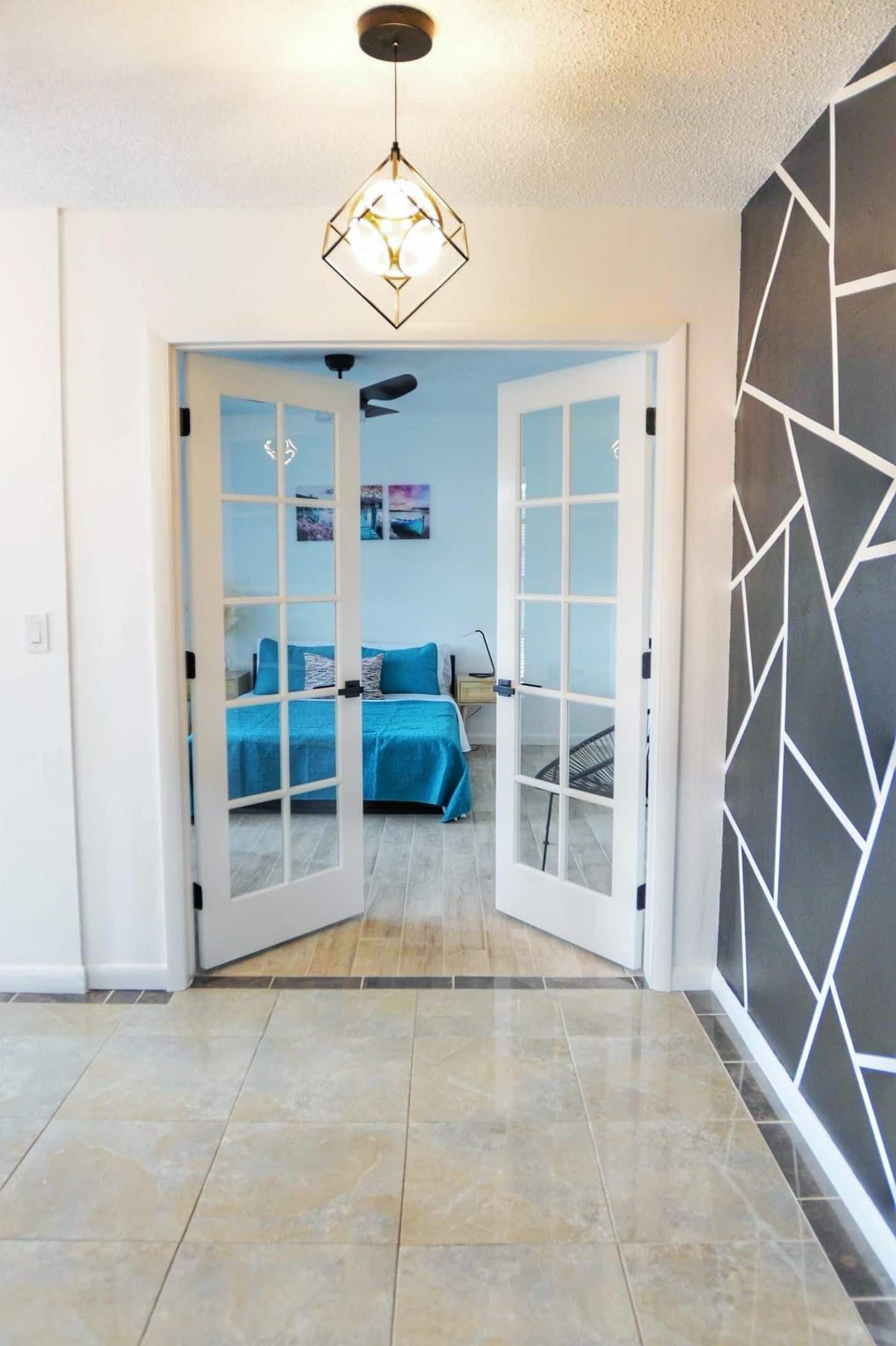 Una habitación con una cama, un escritorio y una silla. Hay una puerta que conduce a otra habitación.