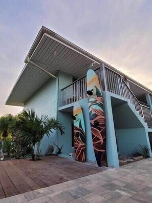Un edificio con un balcón, una gran escultura abstracta y un camino pavimentado.