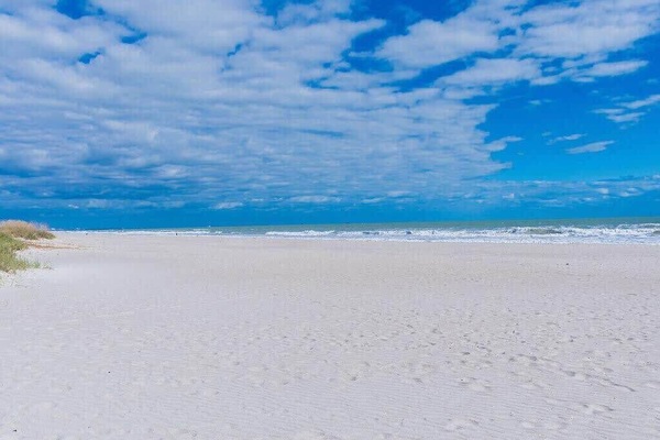 Expansive sandy beach with gentle waves under a partly cloudy sky