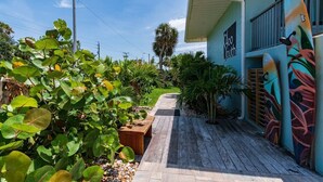 A pathway leading to a building with a mural, surrounded by lush greenery and a clear sky. - 400 South - Unit C (Cocoa Beach)